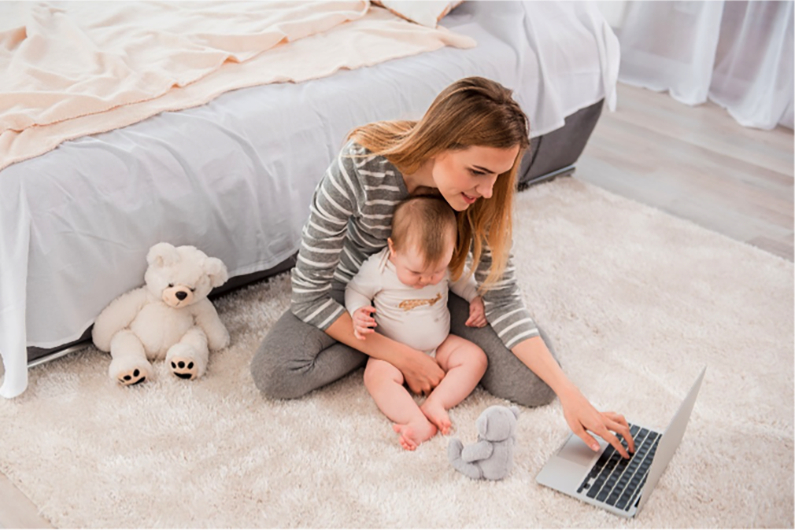 Woman with infant sitting on rug using computer